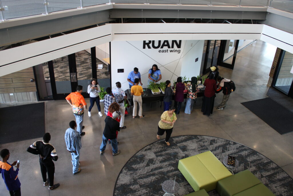 There is a line of students lining up in front of a bamboo planting station. The picture is taken from far away and above. 