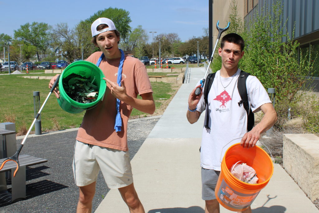 Two boys stand with buckets full of trash. Both are holding grabby tools. 
